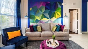 A living room with a modern sofa, a blue armchair, and a coffee table with remotes and a vase. - Walt’s Vision – Disney-Inspired 3BR Condo (Kissimmee)