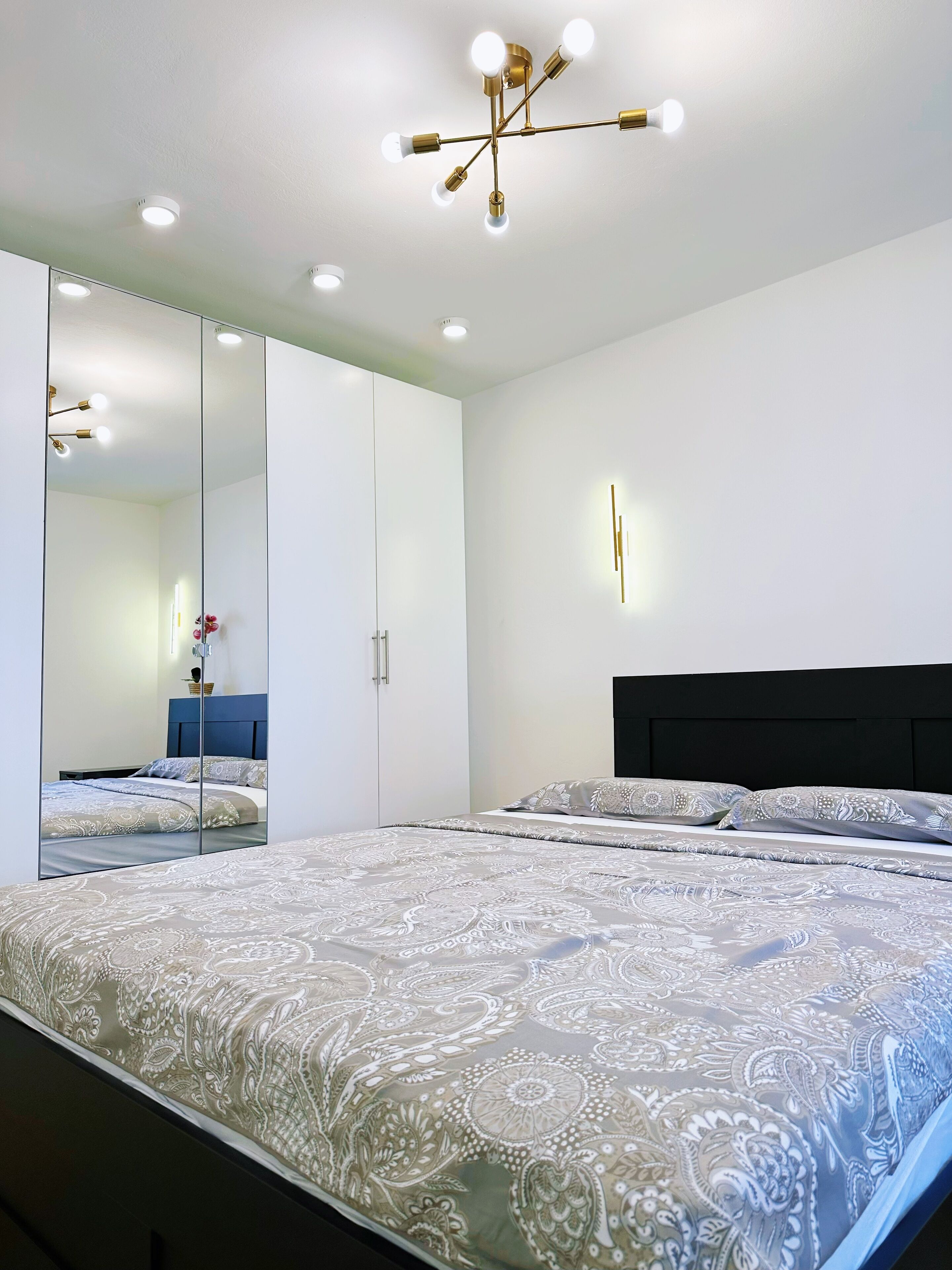 Une chambre moderne avec un grand lit, une armoire à miroir et un luminaire au plafond.