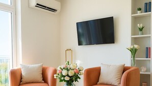 A modern living room with two orange sofas, a round coffee table, and a flat-screen TV mounted on the wall.