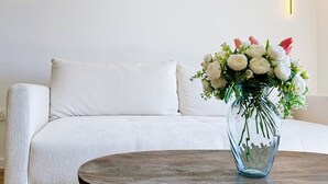 A modern living room with a white sofa, a round wooden coffee table, and a vase with flowers.