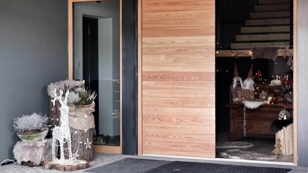 A wooden exterior with a sliding glass door leading to a warmly lit interior. - CASA ESTER (Baselga di Pine)