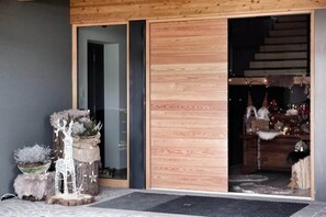 Fachada de madera con puerta corredera de vidrio que da a un interior cálidamente iluminado.