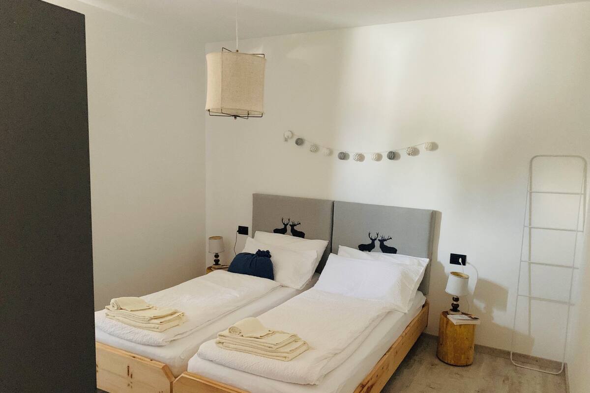 Un lit double avec un cadre en bois, deux tables de chevet avec des lampes, une tête de lit avec un panneau gris et une étagère murale agrémentée d’objets décoratifs.