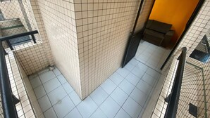 A corner of a room with tiled walls and floor, a metal gate, and a sofa in a corner. - Foot on the sand beach of Guilhermina III (Praia Grande)