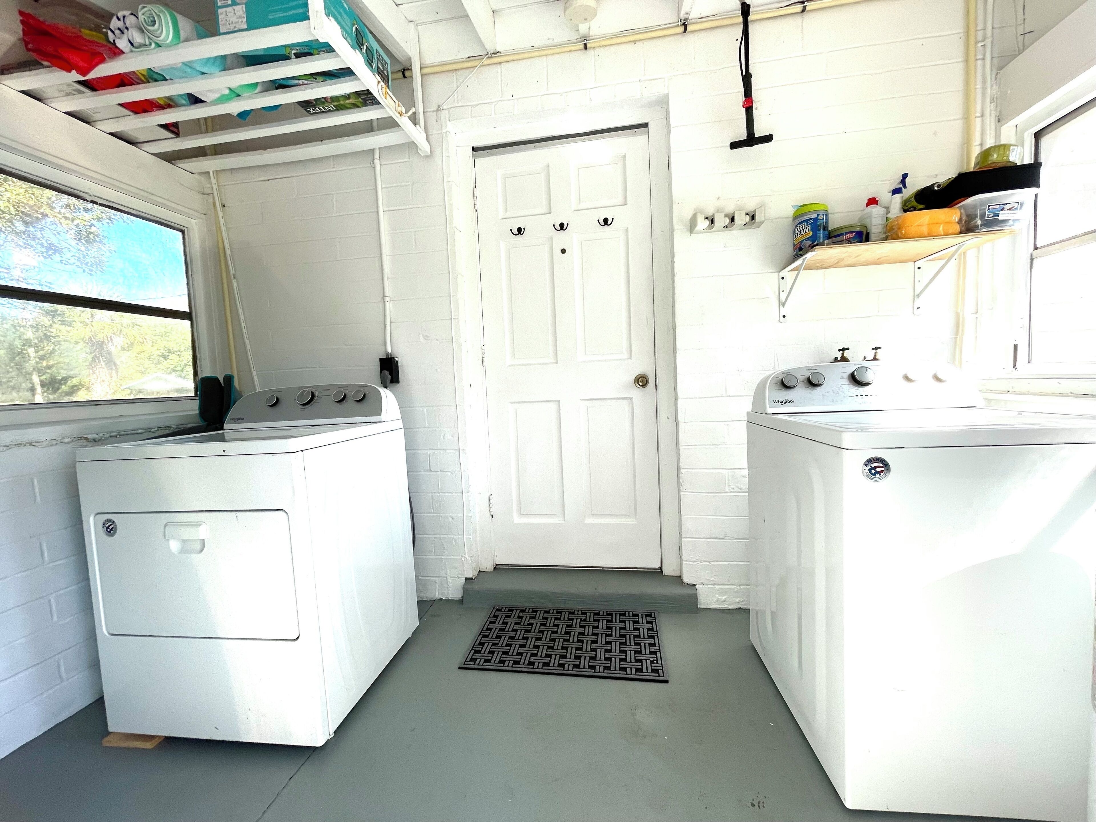 A laundry room with two white washing machines, a white door, and a shelf with cleaning supplies.