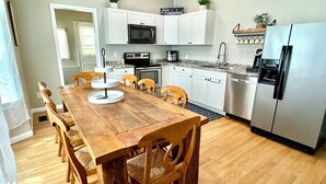 A modern kitchen with white cabinets, a stainless steel refrigerator, a wooden dining table with chairs, and a microwave above the stove. - Burnside Boathouse – Cozy 5 Bedroom Lake Retreat Steps from Marina & Local Eats (Burnside)