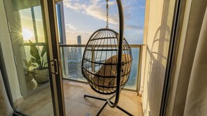 A balcony with a hanging chair, a view of the cityscape, and a potted plant.