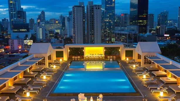 A rooftop pool with lounge chairs and a bar area, surrounded by high-rise buildings.