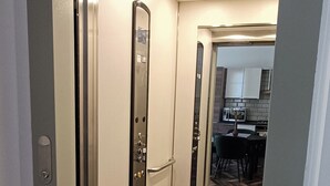 Un couloir étroit et bien éclairé, doté d’un ascenseur moderne et d’un mur miroitant qui reflète un espace salle à manger.