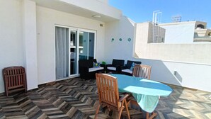 Une terrasse dotée d’un sol en motif de parquet, d’une table avec des chaises et d’une porte-fenêtre coulissante donnant sur un espace intérieur.