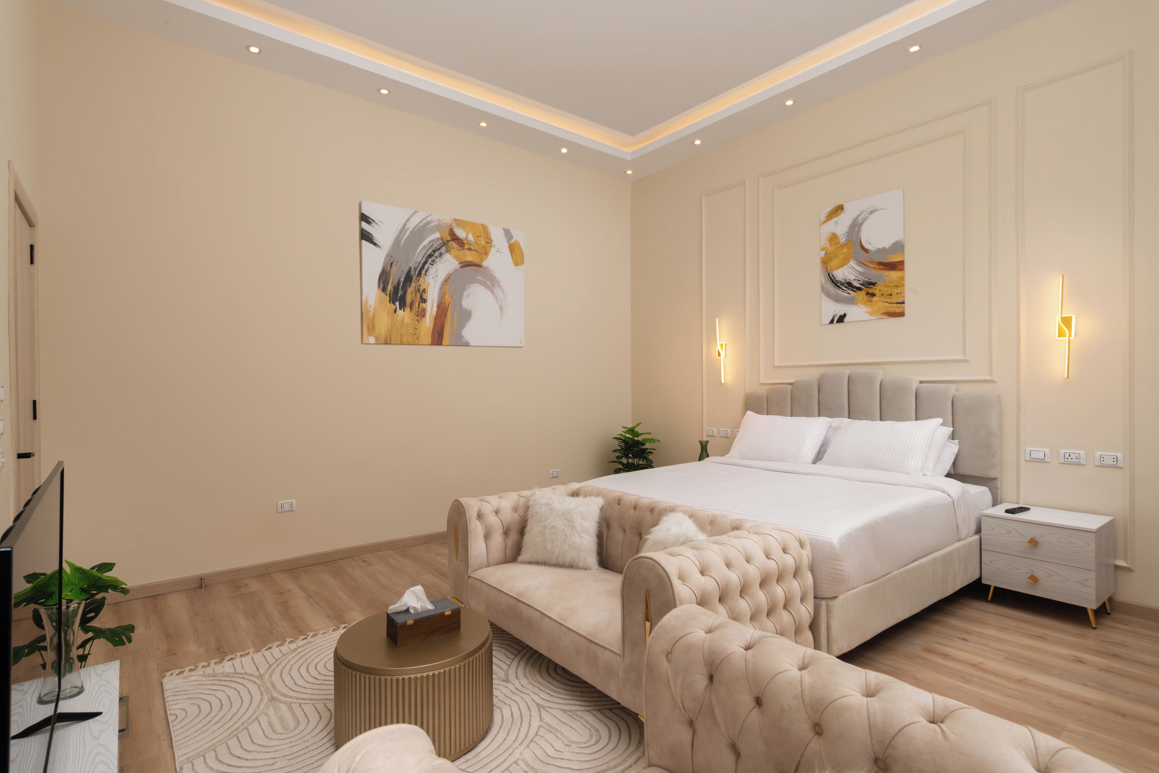A modern bedroom with a large bed, a sofa, a bedside table, and two wall-mounted lamps.