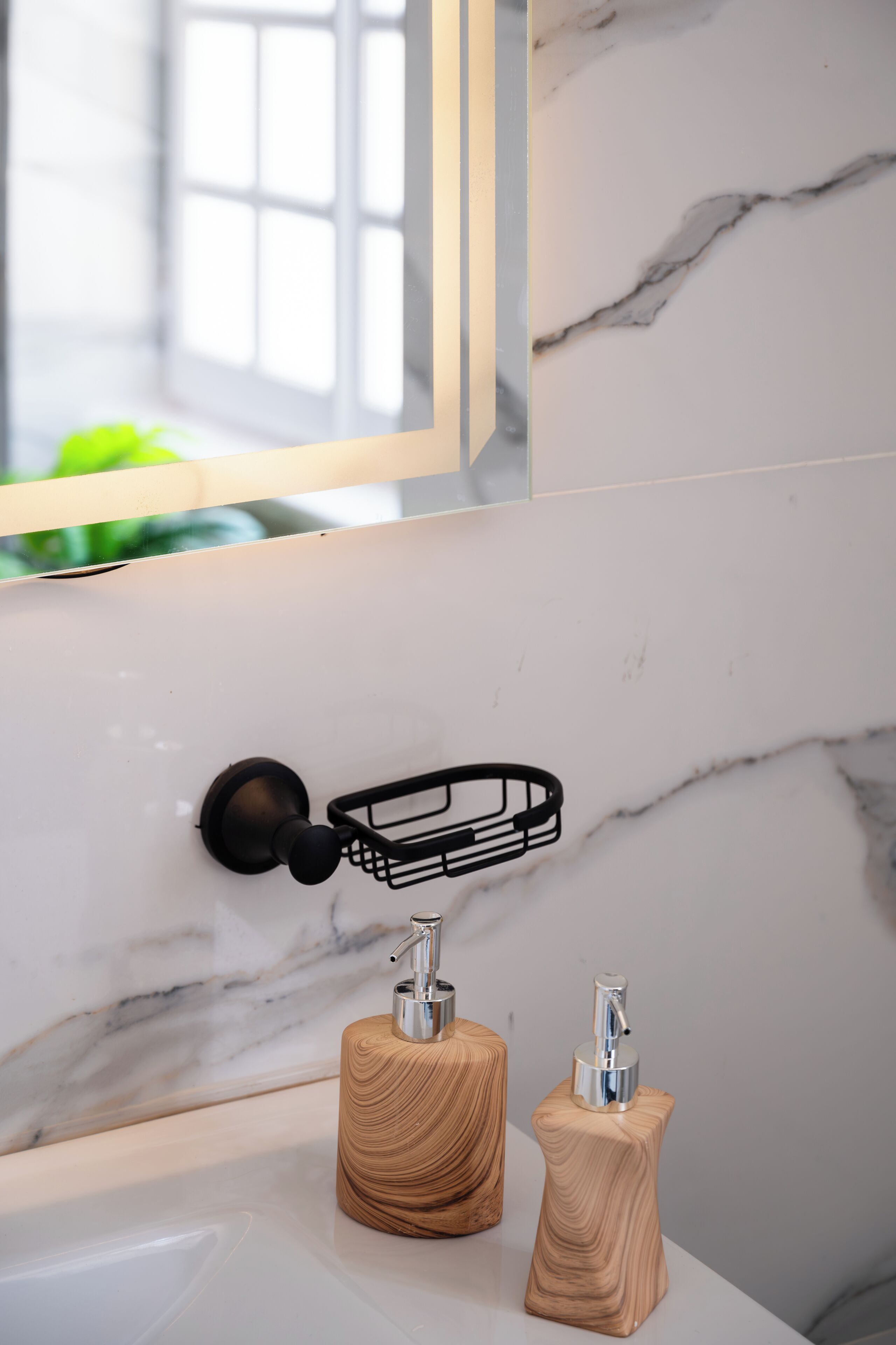 A bathroom with a marble wall, a black towel rack, and two wooden soap dispensers.
