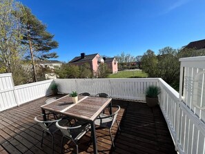A wooden deck with a table and chairs, surrounded by a white fence, with a clear view of a house and trees in the background.