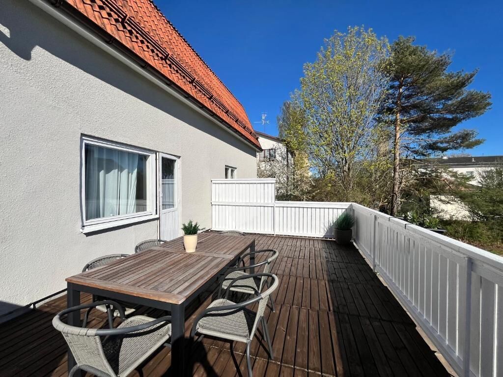 Una terraza de madera con una mesa y sillas, una valla blanca y un árbol al fondo.