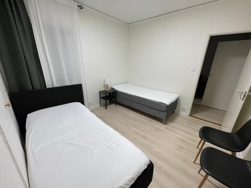 A bedroom with a bed, a bedside table, a chair, and a door leading to another room.