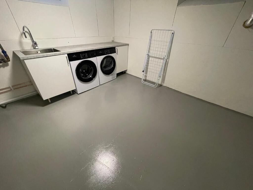 A compact laundry area with a washing machine, a sink, and a drying rack.