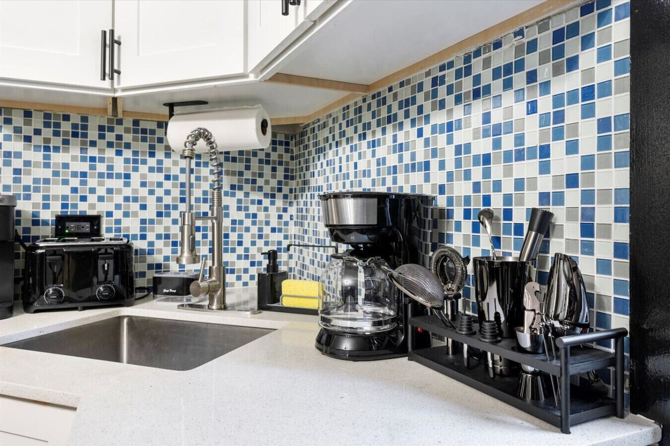 Una cocina con salpicadero de azulejos, una cafetera, un hervidor y un lavabo.