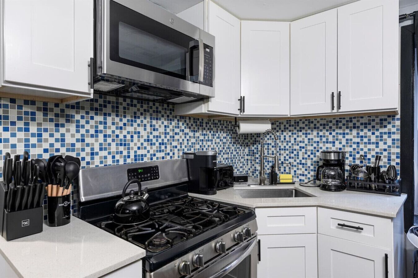 A kitchen with white cabinets, a gas stove, a microwave, and a coffee maker.