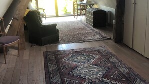 Une pièce mansardée avec un plafond en pente, des poutres apparentes, un bureau, une chaise et un tapis à motifs.