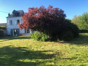 Une maison à deux étages avec un grand arbre devant.