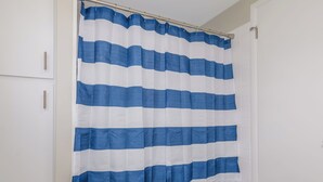Un baño con cortina de ducha azul y blanca a rayas, suelo de madera y puerta blanca.