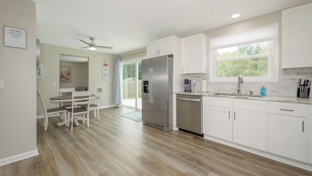 Una cocina moderna con armarios blancos, un refrigerador de acero inoxidable y una zona de comedor con mesa y sillas.