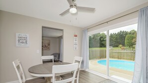 Un comedor con una mesa redonda y cuatro sillas, un ventilador de techo y vista a un patio trasero con piscina.