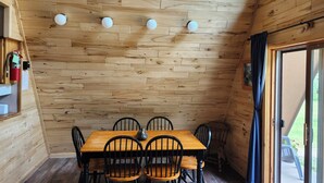 Ein Zimmer mit Holzwänden, einem Tisch, Stühlen, einem Feuerlöscher und einem Fenster mit Vorhängen.