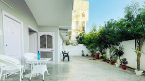 A courtyard with white wicker furniture, potted plants, and a door leading to an interior space. - Dormtales Hostel (Varanasi)