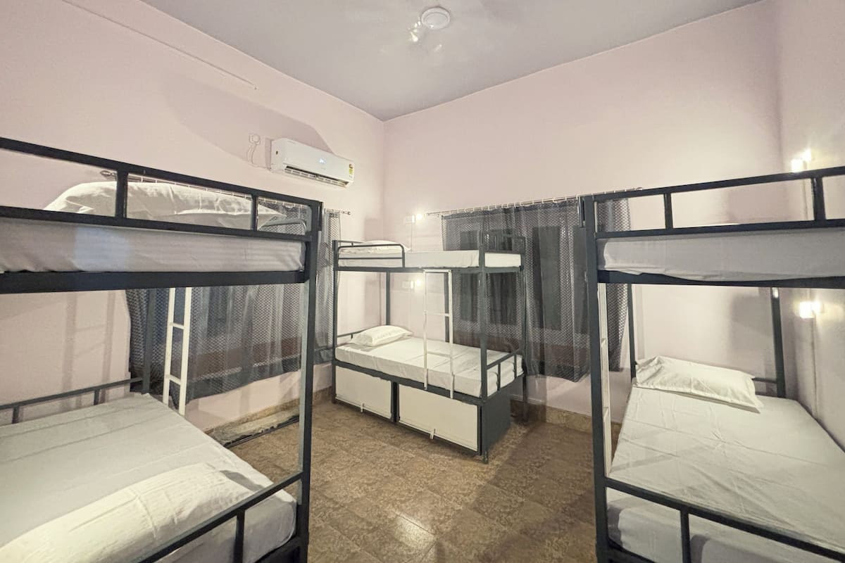 A dormitory room with bunk beds, an air conditioning unit, and a window with curtains.