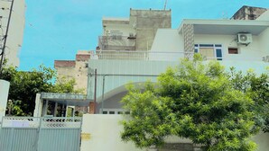 A residential building with a gated entrance, a balcony, and a tree in the foreground. - Dormtales Hostel (Varanasi)