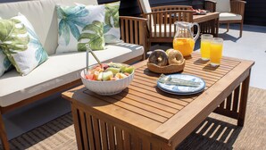 A wooden table with breakfast items, a bowl of fruit, and a pitcher of orange juice on a rooftop terrace with a view of the city skyline. - Seaside Zen Retreat 4-bedroom house in beautiful Seaside Heights with AC, WiFi (Seaside Heights)