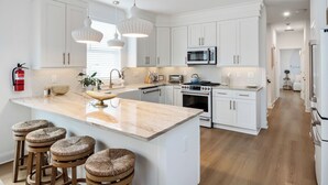 A modern kitchen with white cabinets, a central island with stools, a microwave, stove, and a fire extinguisher. - Seaside Zen Retreat 4-bedroom house in beautiful Seaside Heights with AC, WiFi (Seaside Heights)