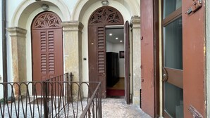 A building entrance with two large wooden doors, a metal gate, and a staircase leading inside. - Aure (Verona)