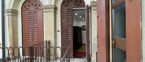 A building entrance with two large wooden doors, a metal gate, and a staircase leading inside.