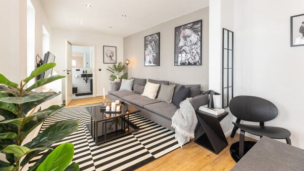 Una sala de estar moderna con un sofá gris, alfombra a rayas blanco y negro, y una mesa de centro negra con velas.