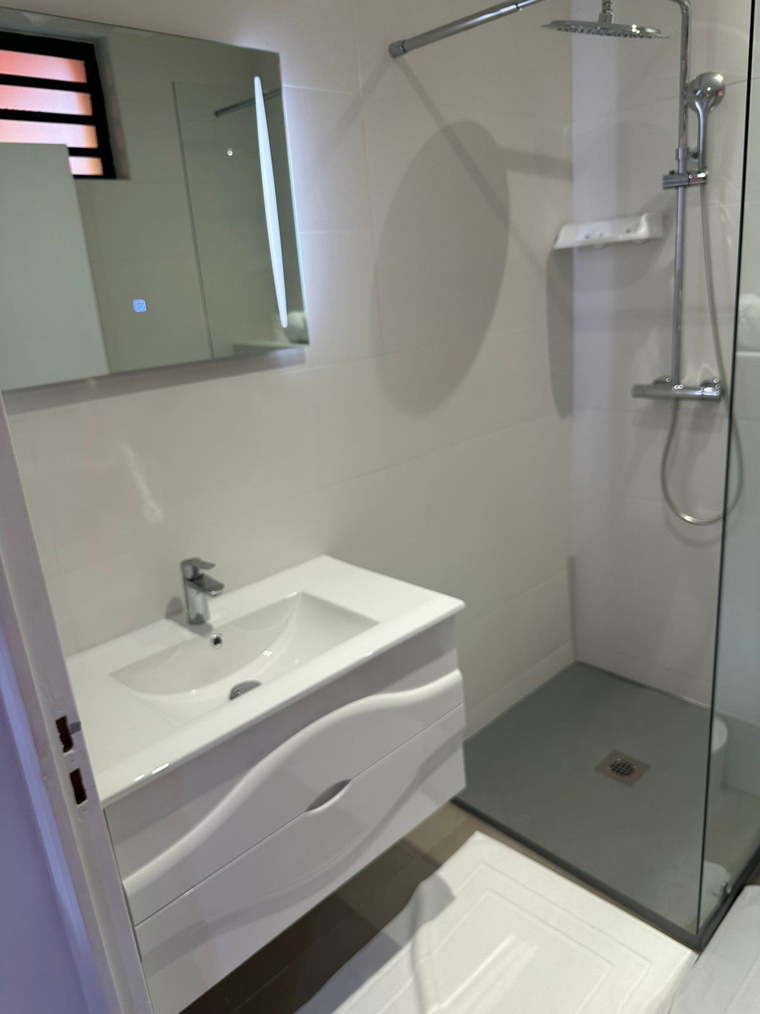 Une salle de bain moderne avec une douche à parois de verre, un lavabo blanc et un grand miroir.
