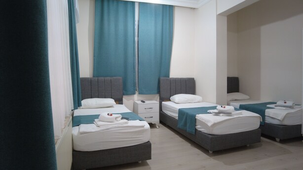 A hotel room with two single beds, a small bedside table, and a large window with curtains. - Odak Pansiyon (Çanakkale)