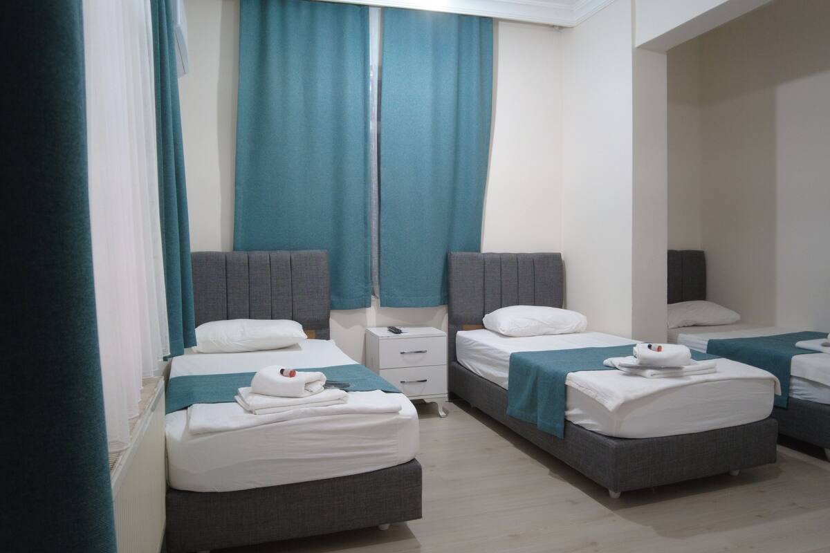 Une chambre d’hôtel avec deux lits simples, une petite table de chevet et une grande fenêtre avec des rideaux.