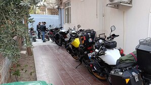 A row of motorcycles parked outside a building with a tiled floor and a few people standing nearby. - Odak Pansiyon (Çanakkale)