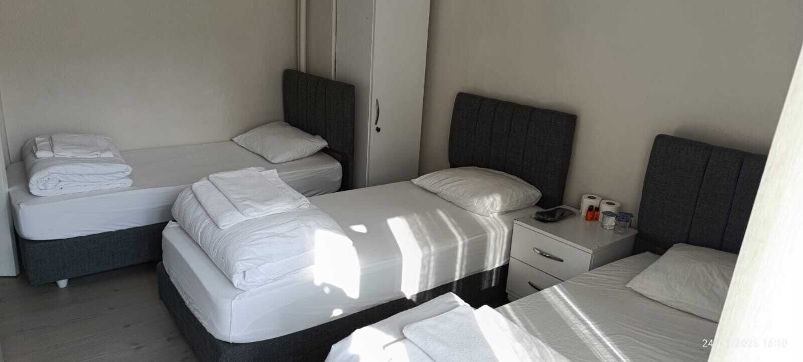 A hotel room with two single beds, a small bedside table with a lamp, and a nightstand with a phone and toiletries.