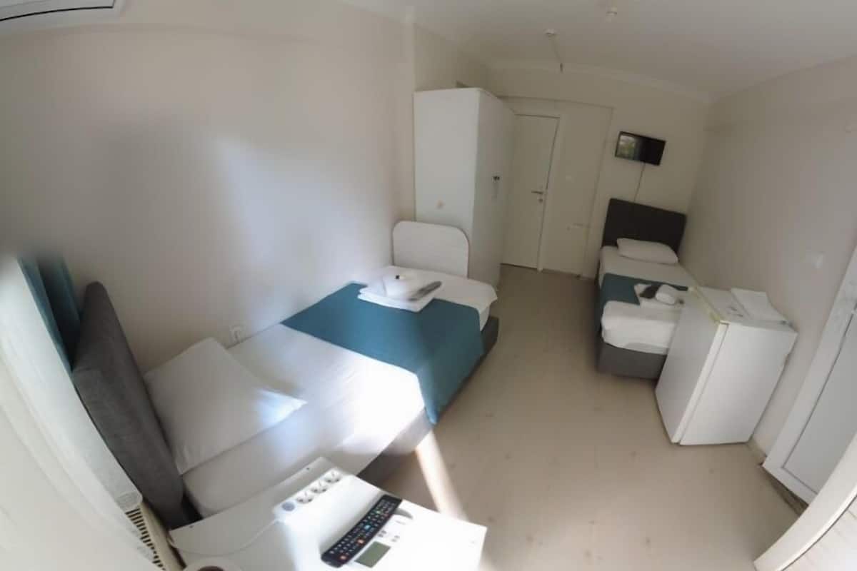 Une petite chambre d’hôtel avec un lit simple, un bureau avec un ordinateur, une chaise, une armoire et un petit réfrigérateur.