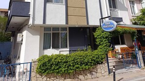 A multi-story building with balconies, a sign reading 'ODAK PANSIYON,' and a stone wall with greenery in front. - Odak Pansiyon (Çanakkale)