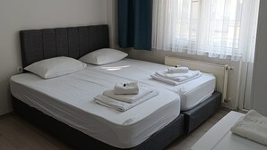 A double bed with white linens, a dark headboard, and a bedside table with a towel. - Odak Pansiyon (Çanakkale)