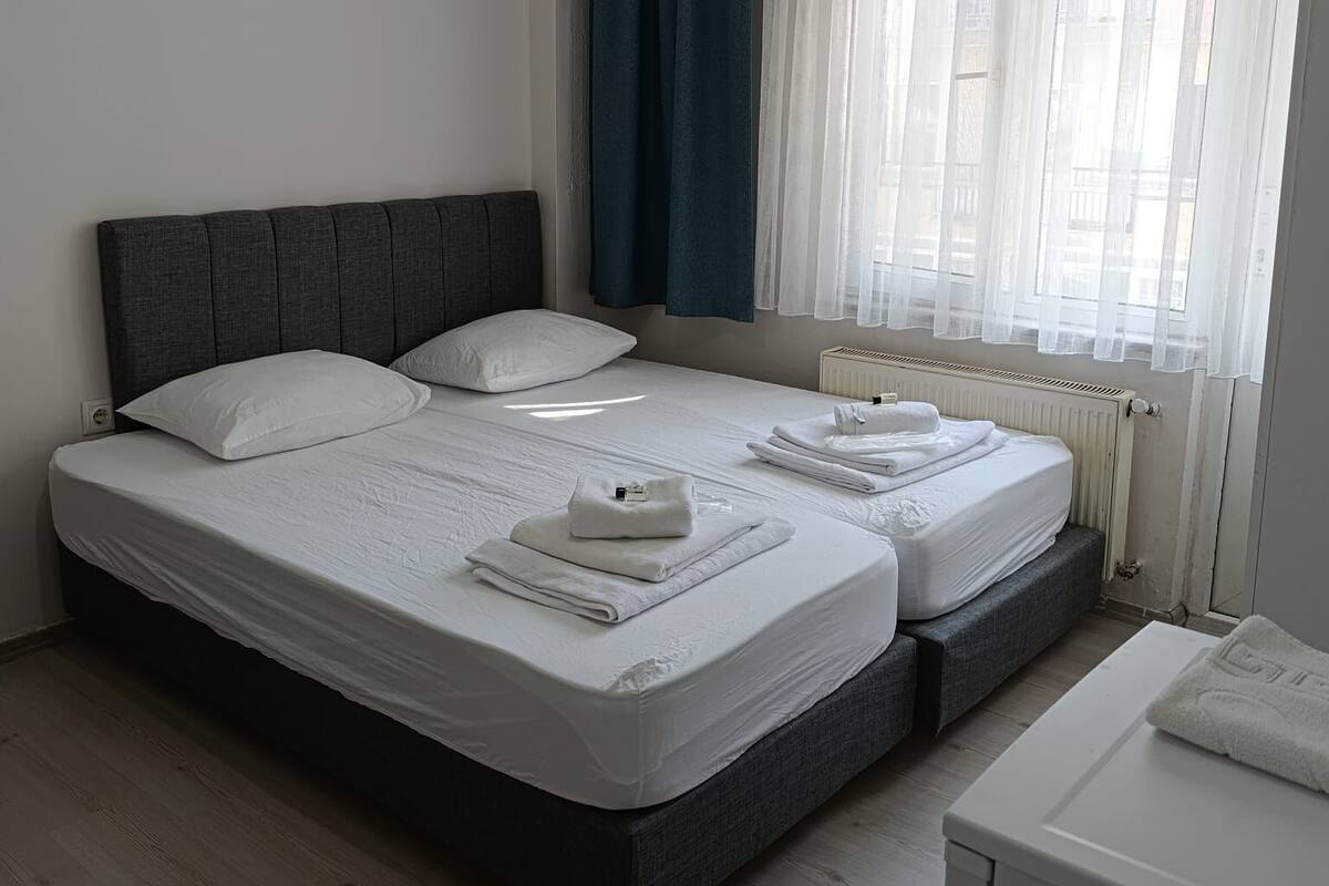 Un lit double avec du linge de lit blanc, une tête de lit sombre et une table de chevet avec une serviette.