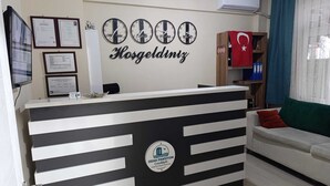 A reception desk with a black and white striped design, a wall clock, framed certificates, and a Turkish flag. - Odak Pansiyon (Çanakkale)
