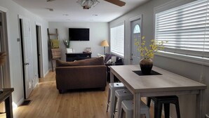A modern living room with a sofa, a dining table, and a TV mounted on the wall. - Waterfront Cottage w/ boat dock

 (Blenheim)