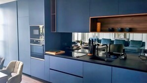 A modern kitchen with blue cabinetry, a dining area with a table and chairs, and a built-in oven.