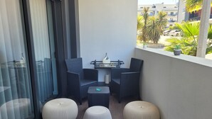 Un balcón con mobiliario de mimbre, que incluye dos sillones y una mesita, junto con tres otomanes redondos.