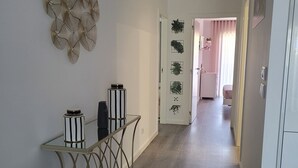 Un pasillo con comedor que incluye una mesa de vidrio y sillas de metal, un adorno en la pared y una puerta que da a otra habitación con paredes rosadas.